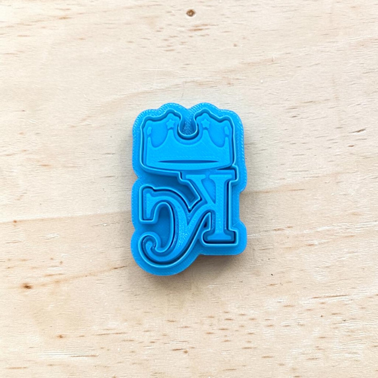 Blue cookie cutter with star crowned KC design on a wooden surface