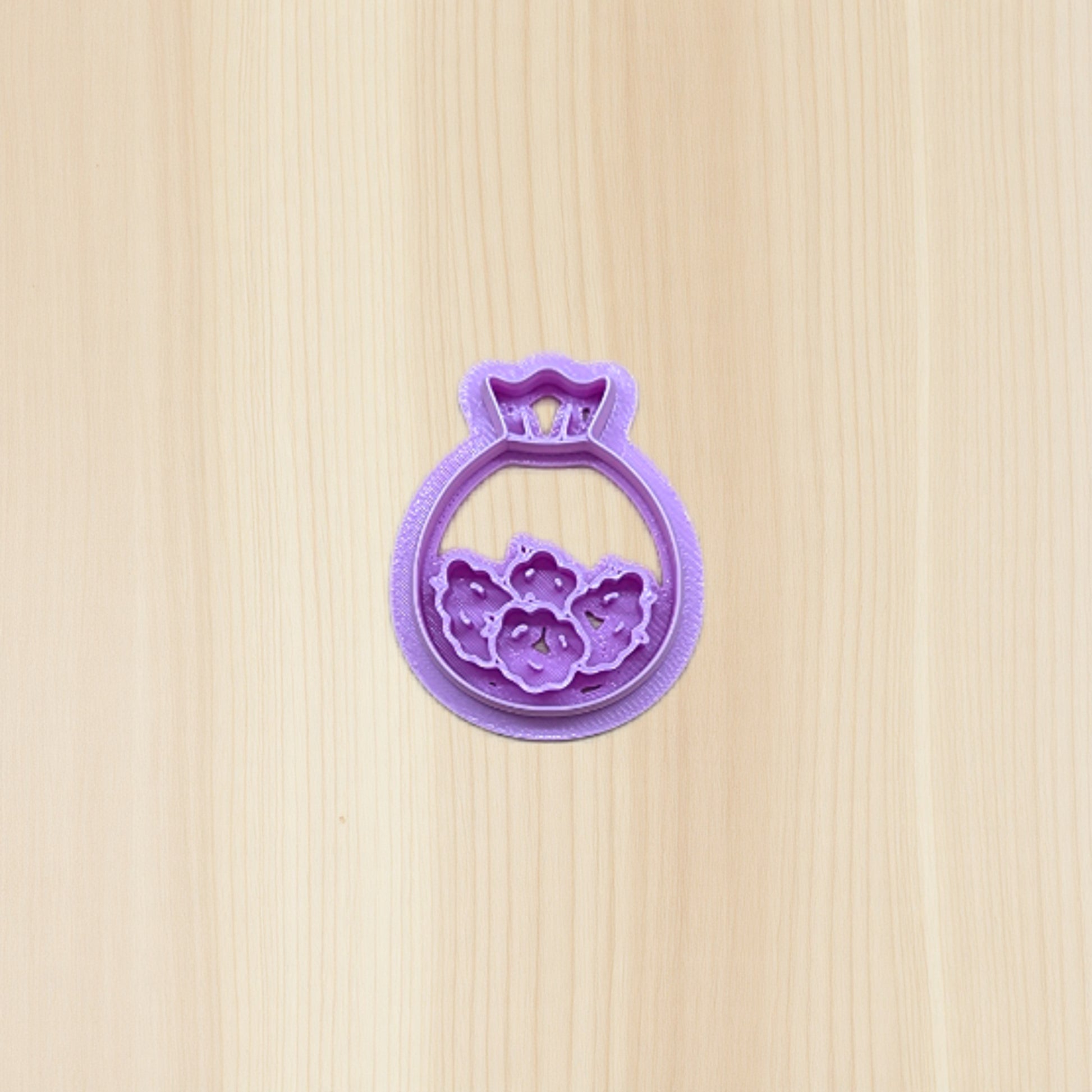 Purple plastic cookie cutter shaped like a bag of cannabis buds on a wooden surface