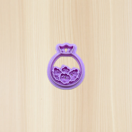 Purple plastic cookie cutter shaped like a bag of cannabis buds on a wooden surface