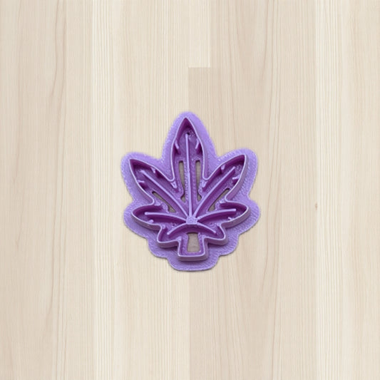 Purple cannabis leaf-shaped cookie cutter on a light wood surface