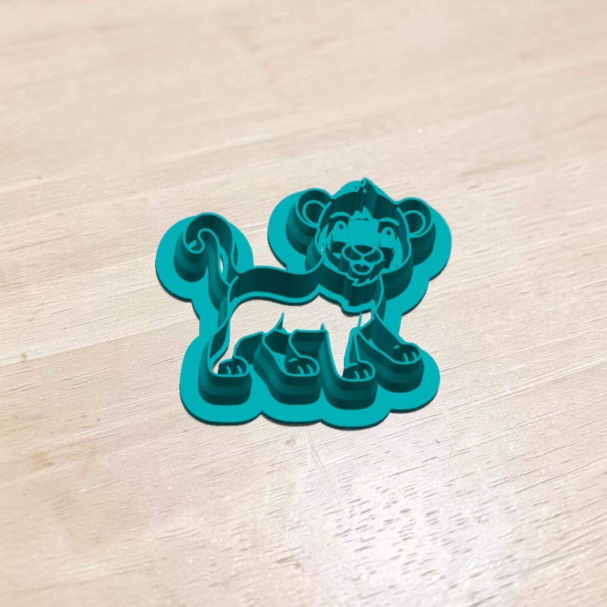 Turquoise 3D printed Cute Lion Cub Cookie Cutter featuring a smiling baby lion with a curly tail, detailed mane and paws for safari cookies, polymer clay earrings, fondant, pottery and ceramic crafts.