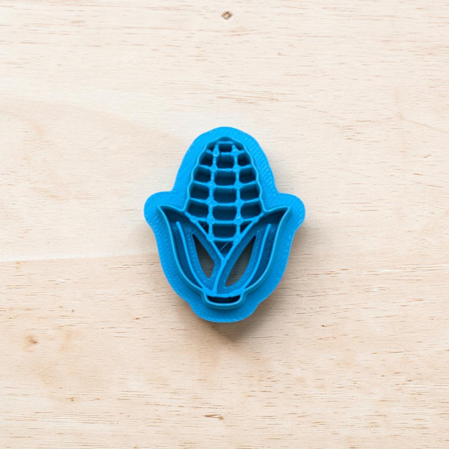 Blue corn-shaped cookie cutter on a light wooden surface