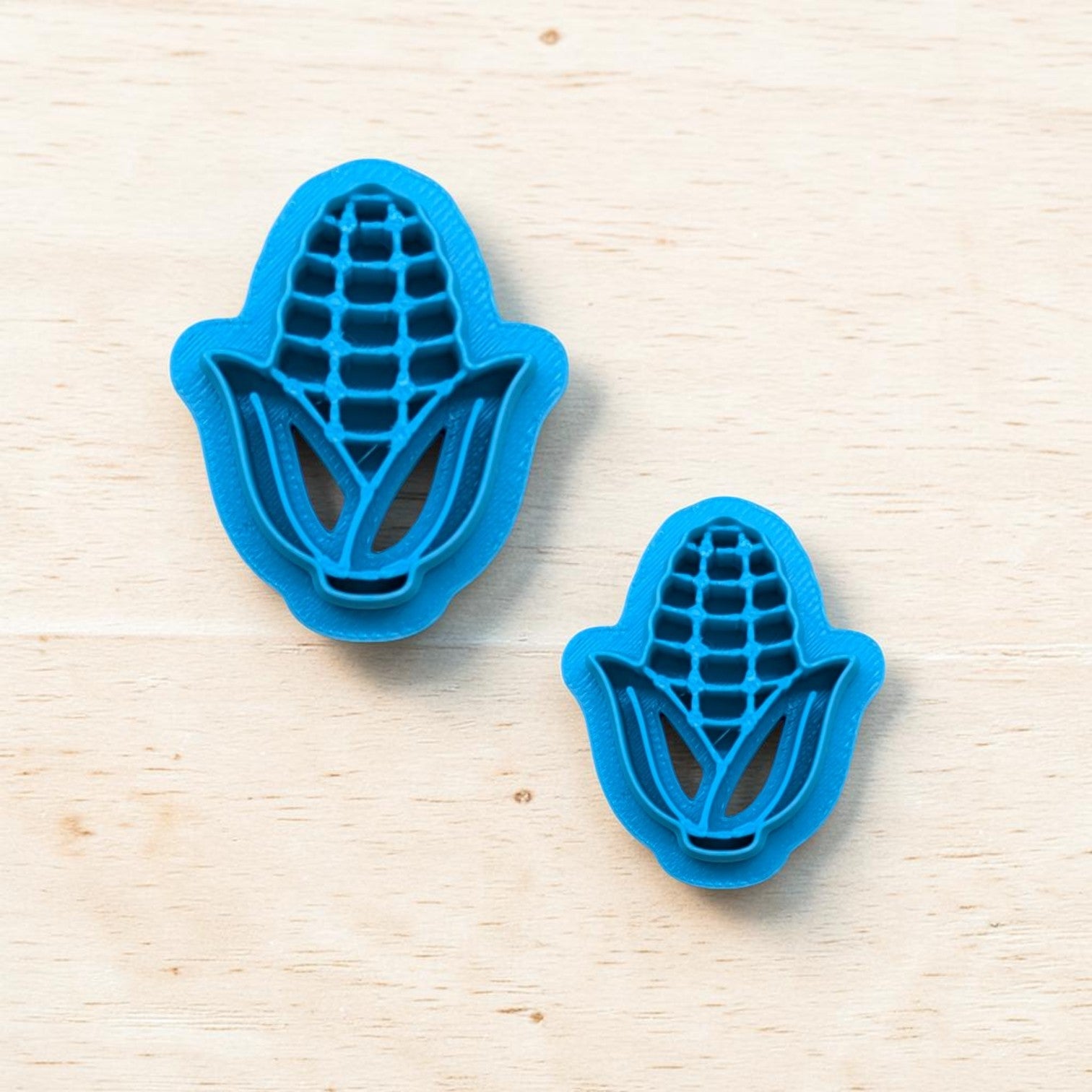 Two blue corn-shaped cookie cutters on a light wooden surface