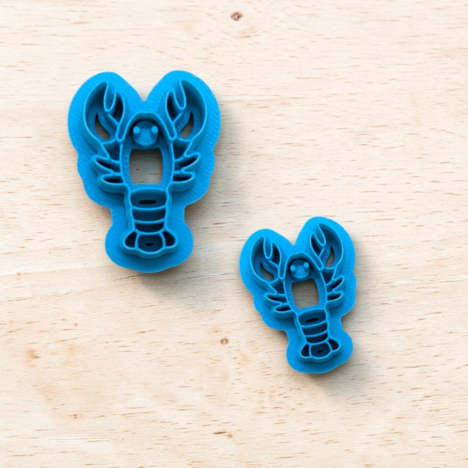 Two blue lobster-shaped cookie cutters on a wooden surface