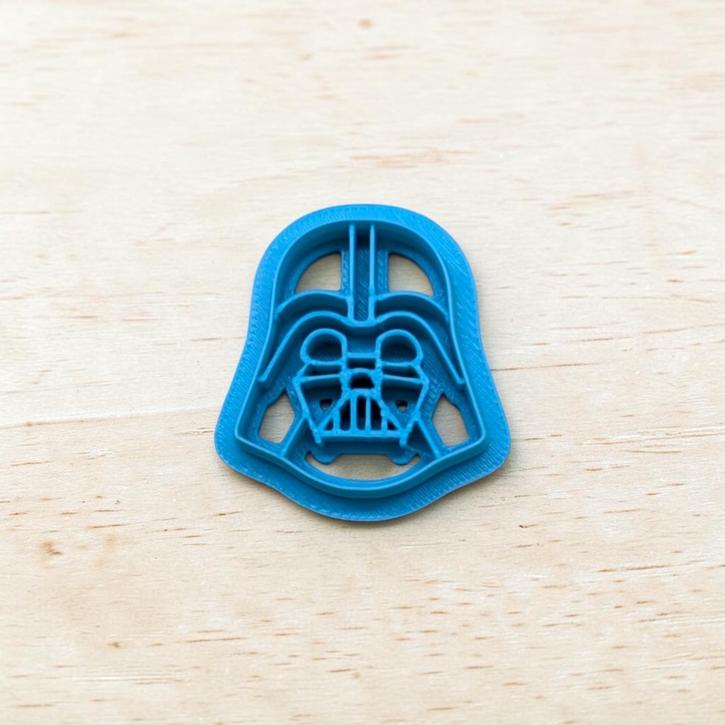 Plastic Darth Vader cookie cutter on a light color wood surface.