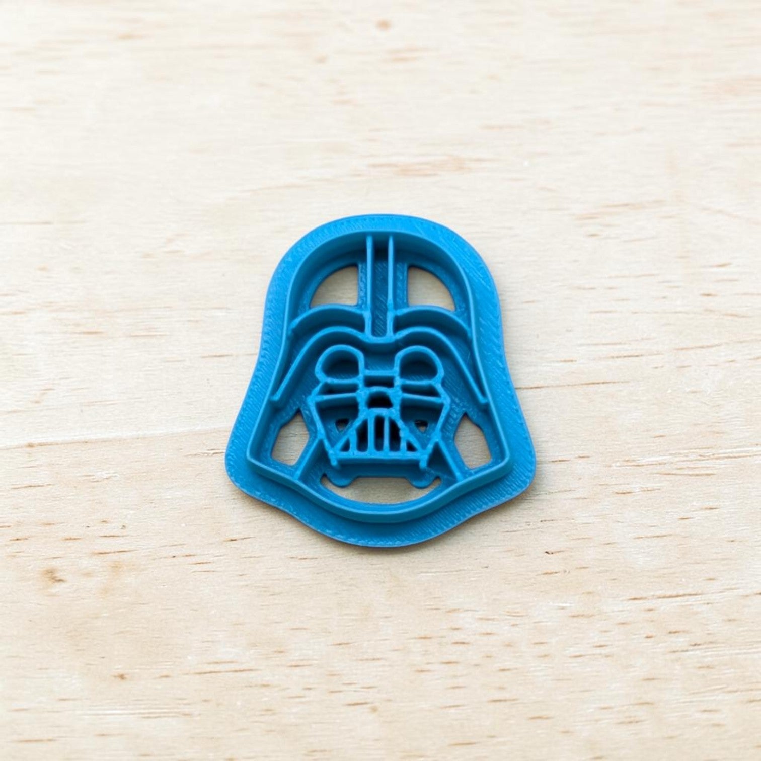 Plastic Darth Vader cookie cutter on a light color wood surface.