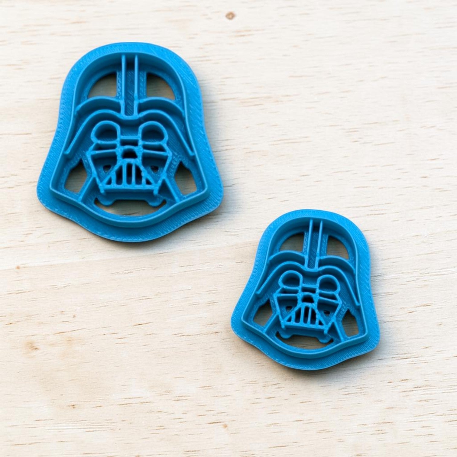 Two blue Darth Vader cookie cutters on a light wooden surface