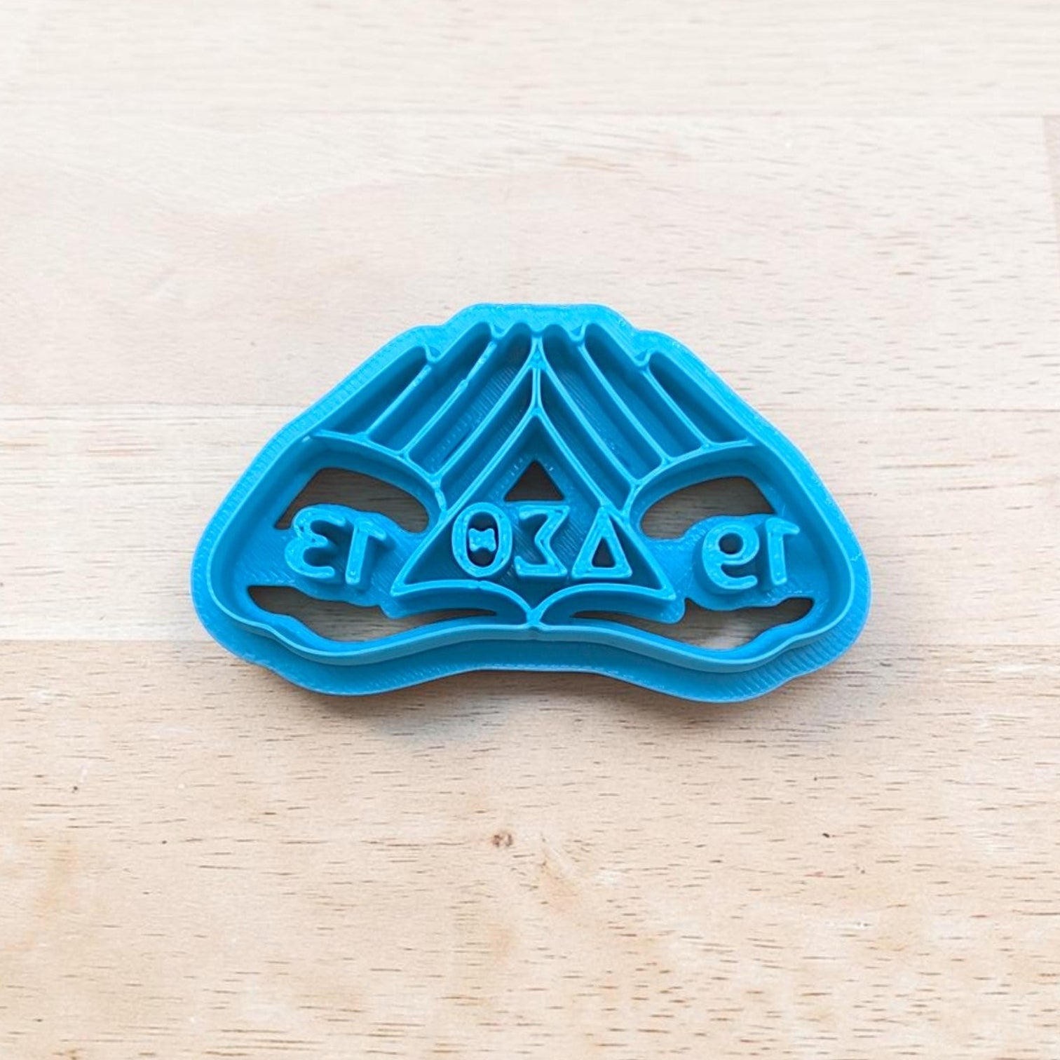 Blue cookie cutter with delta sigma theta hand design on a light wooden surface