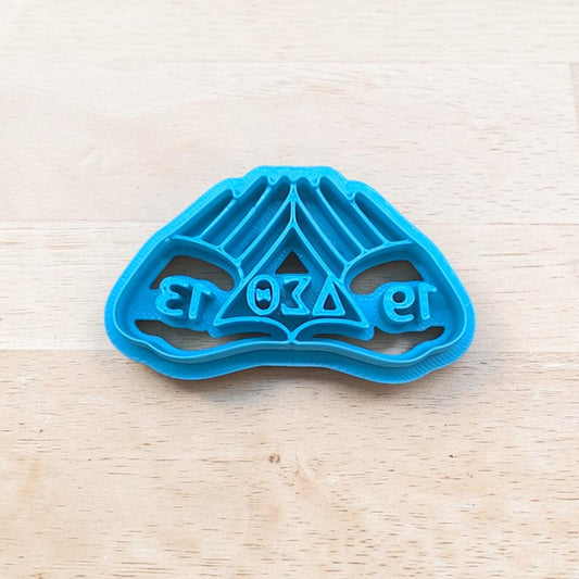 Blue cookie cutter with delta sigma theta hand design on a light wooden surface