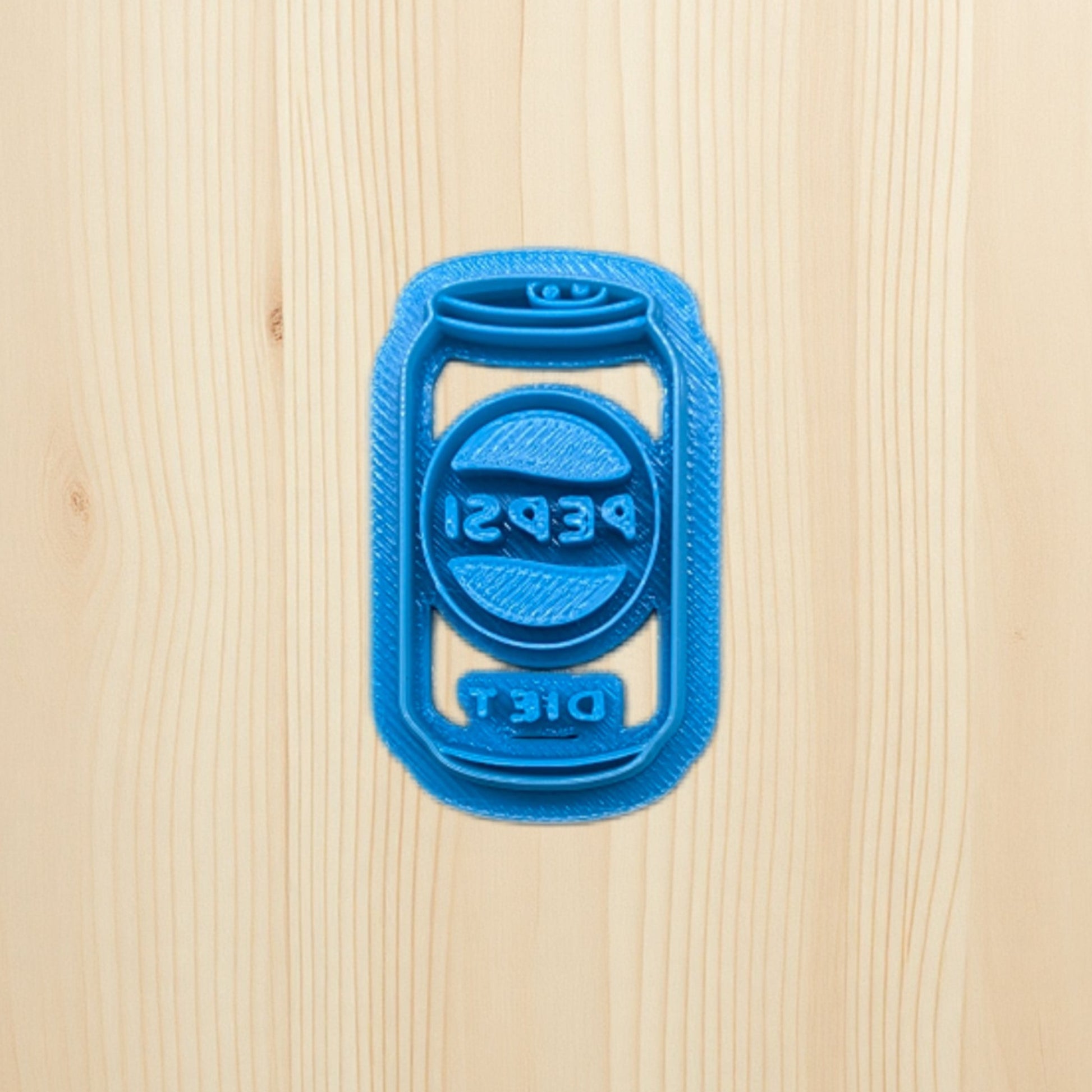 Blue 3D-printed Pepsi soda can cookie cutter on a wooden surface