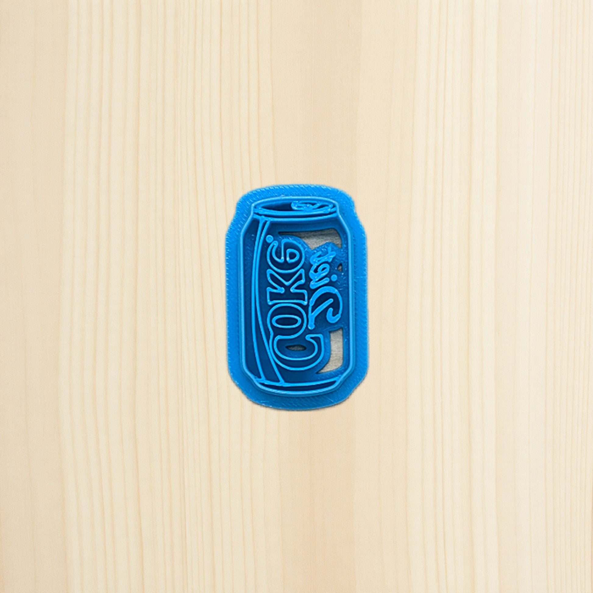 Diet Coke soda pop can cookie cutter laying on wood surface