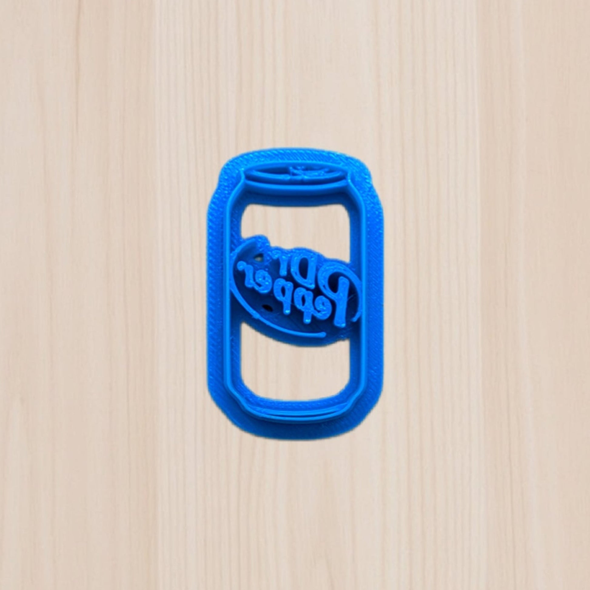Blue, plastic, 3D Printed Dr Pepper soda can cookie cutter on a beige wooden surfaced 