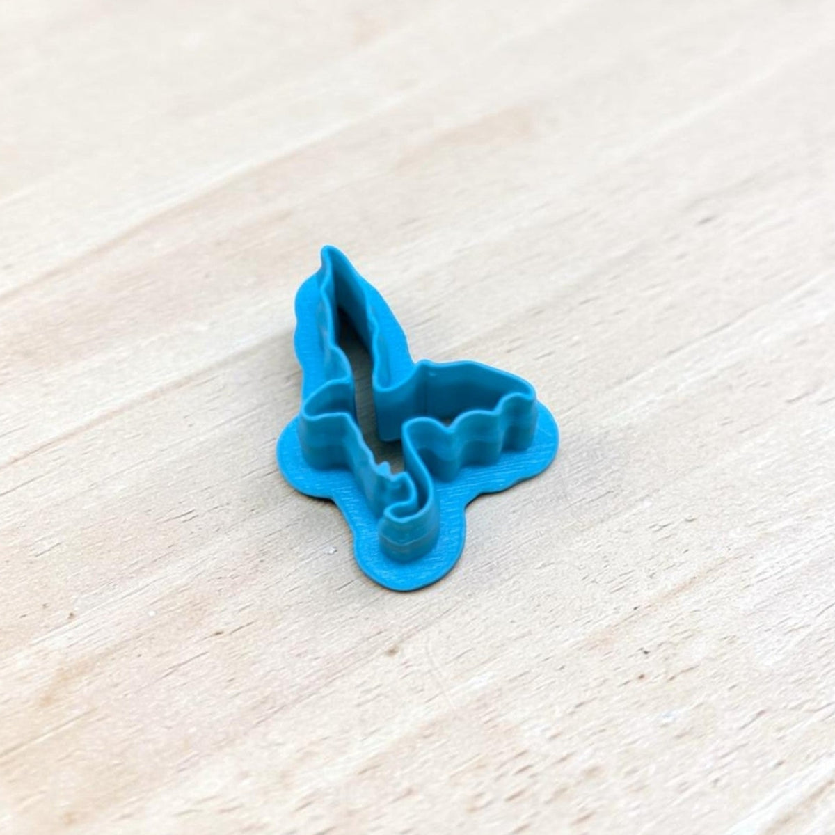 Blue 3D-printed Dragon Silhouette Style E cookie cutter featuring an upright pointed wing, detailed curved edges and a curled tail, photographed on light wood for fantasy cookies, polymer clay earrings, fondant and crafts.