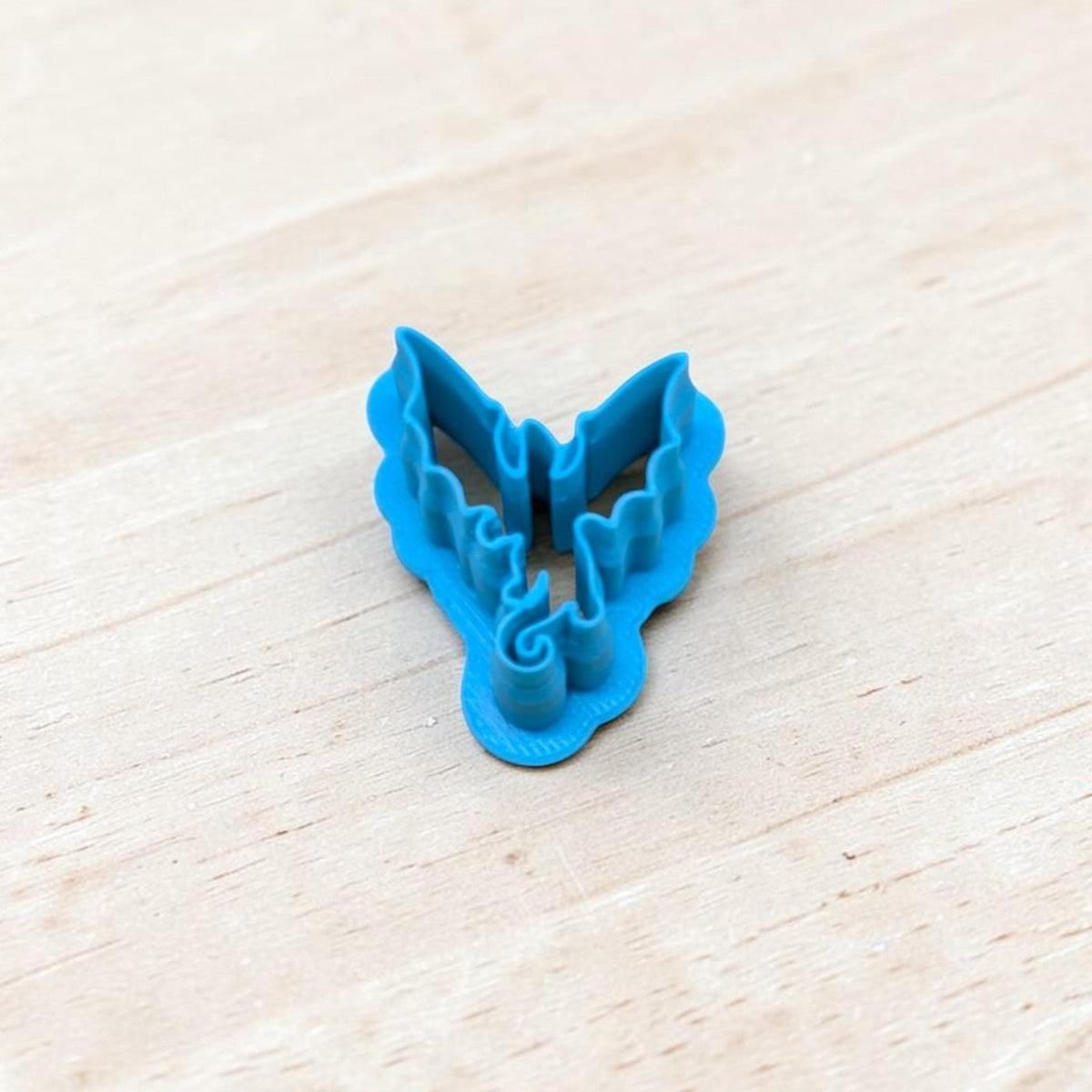 Blue 3D-printed Dragon Silhouette Style F cookie cutter featuring pointed wings, detailed wing edges and a curled tail, photographed on light wood for fantasy cookies, polymer clay earrings and fondant crafts.
