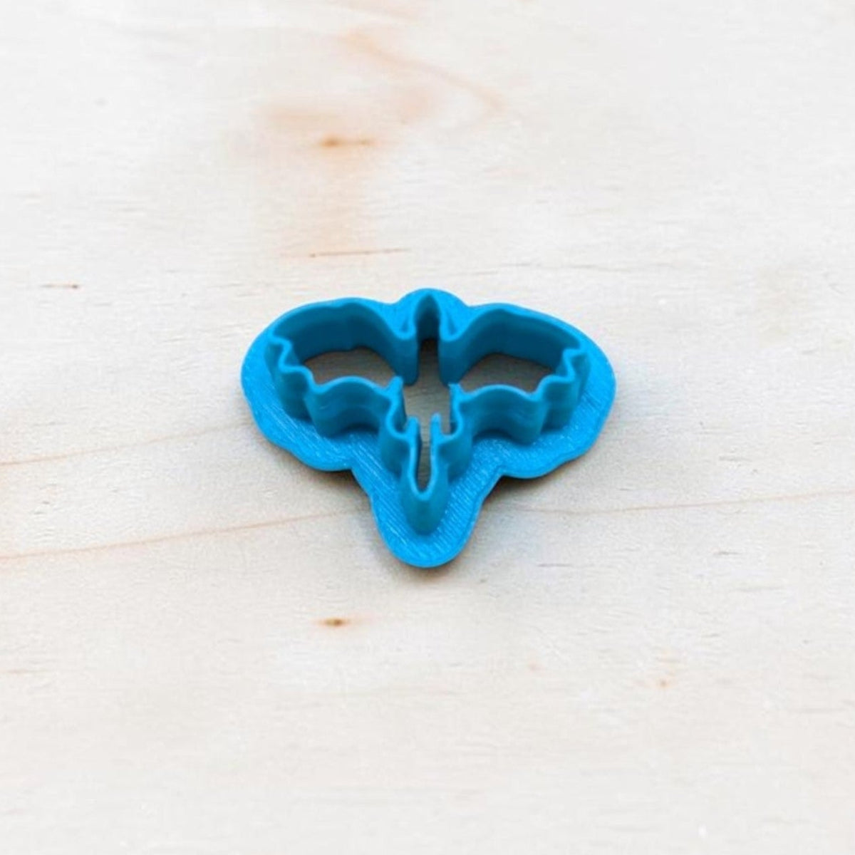 Blue 3D-printed Dragon Silhouette Style D cookie cutter featuring wide, outstretched wings and a pointed tail, photographed on light wood for fantasy cookies, polymer clay earrings, fondant and crafts.