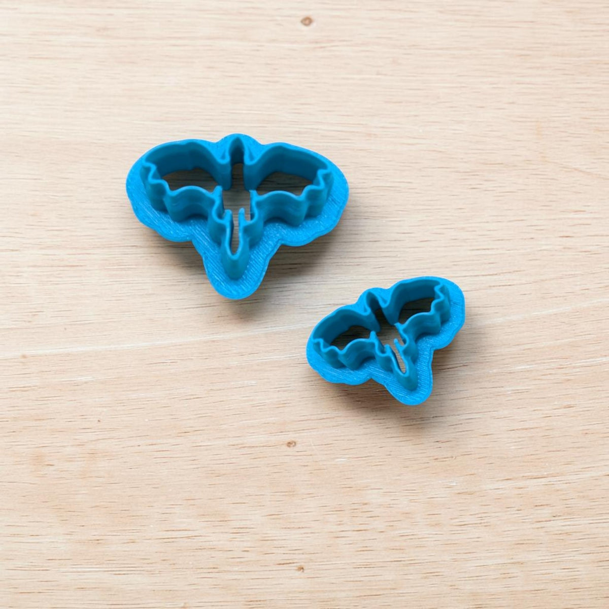 Two blue 3D-printed Dragon Silhouette Style D cookie cutters in different sizes, featuring outstretched wings and pointed tails for fantasy cookies, polymer clay jewelry, fondant and pottery crafts.