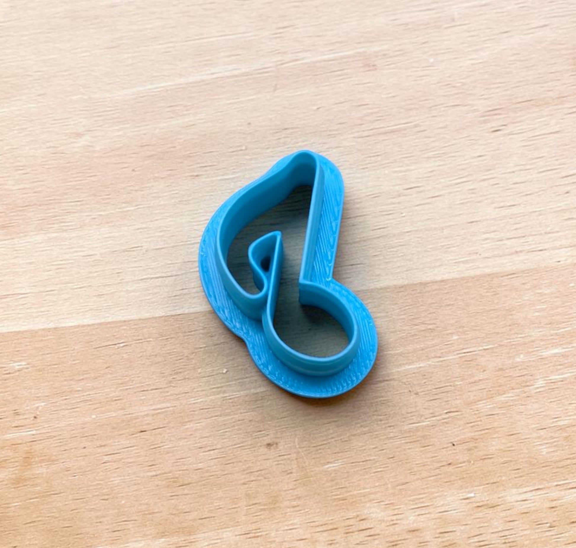 Blue 3D printed eighth note cookie cutter for polymer clay, fondant, and pottery crafts on wood surface