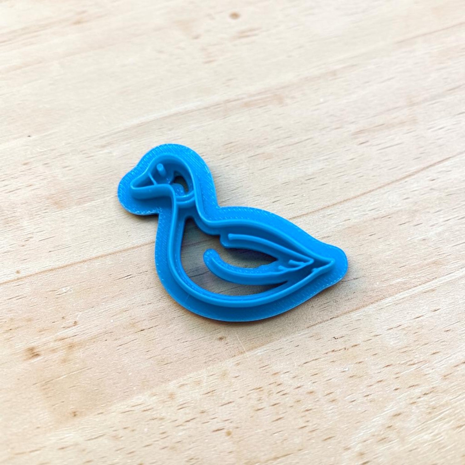 Blue cookie cutter shaped like a duck on a wooden surface