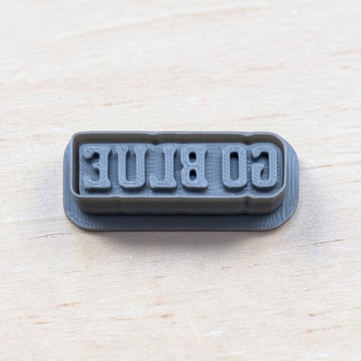 GO BLUE cookie embossing stamp for fondant, polymer clay, or cookies — 3D printed gray stamp showing reversed text for clear imprint.