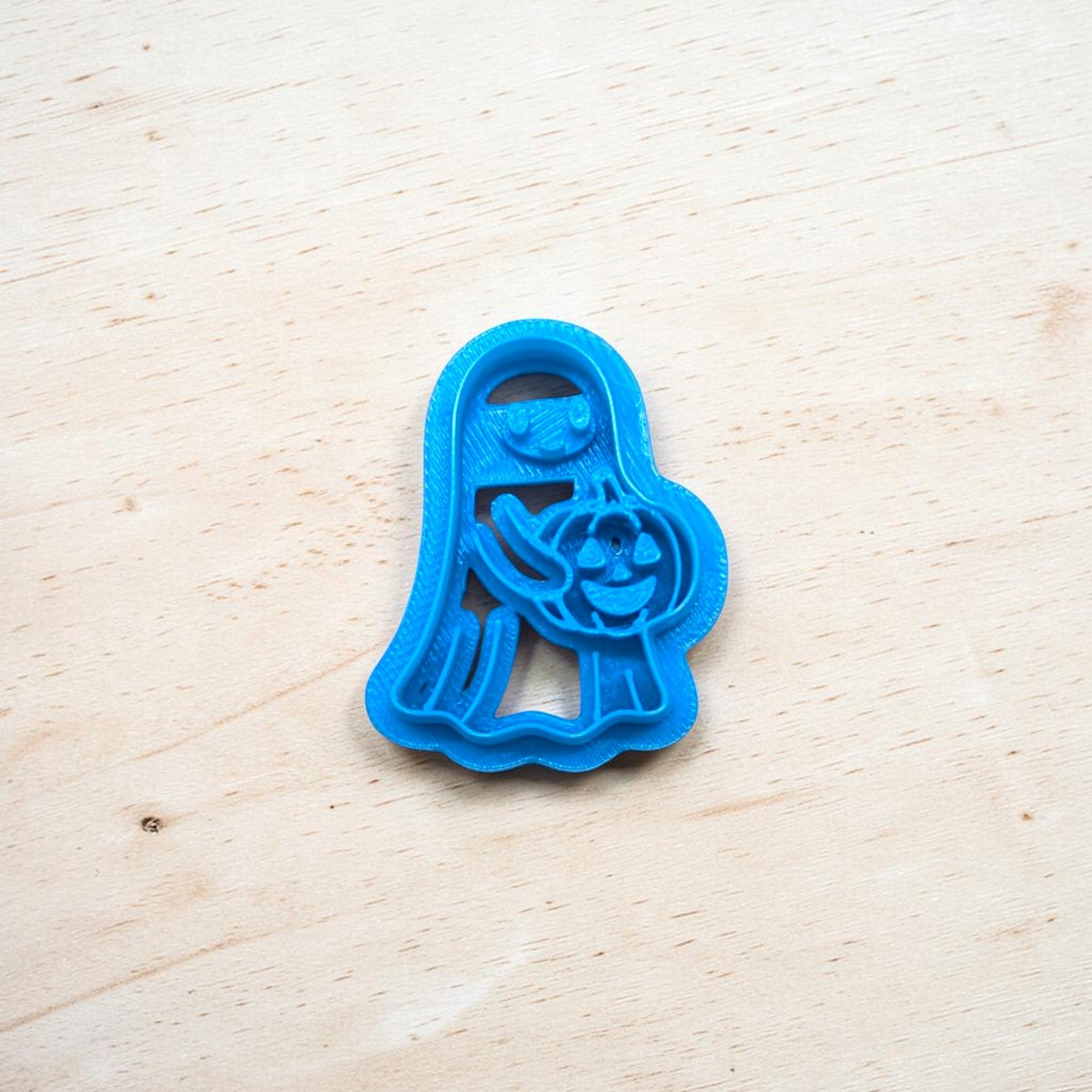Blue cookie cutter shaped like a ghost on a wooden surface