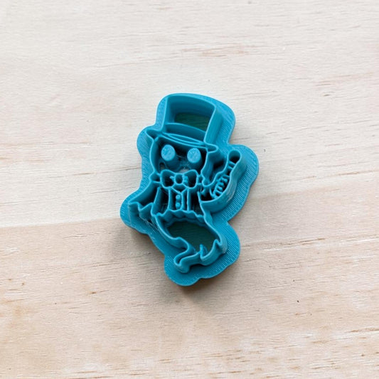 Blue cookie cutter shaped like a ghostly ringmaster wearing a top hat and bow tie, holding a cane, on a light wooden surface.