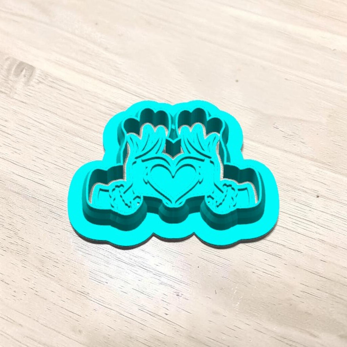 Turquoise 3D-printed Grinch Heart Hands cookie cutter with matching embossing stamp nested inside, showing detailed furry hands forming a heart for Christmas sugar cookies, polymer clay earrings, fondant and crafts.