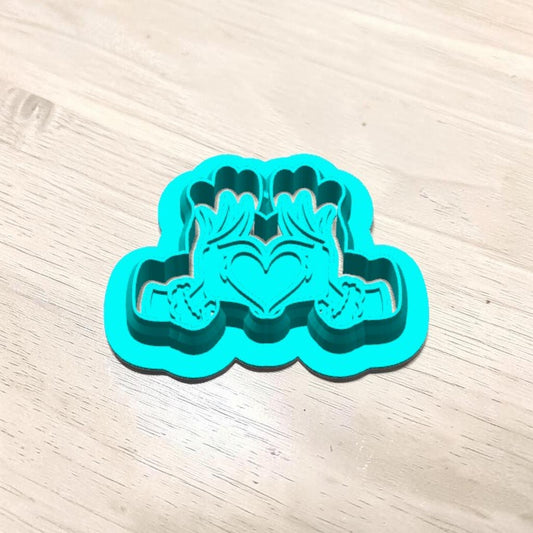 Turquoise 3D-printed Grinch Heart Hands cookie cutter with matching embossing stamp nested inside, showing detailed furry hands forming a heart for Christmas sugar cookies, polymer clay earrings, fondant and crafts.
