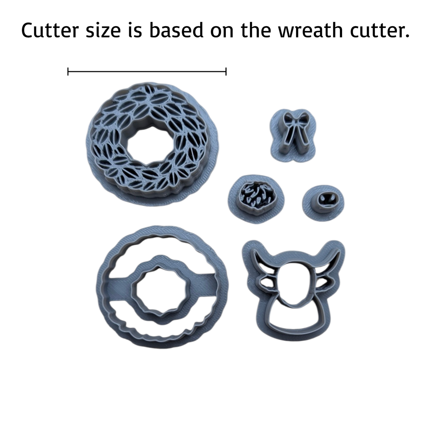 A set of gray plastic cookie cutters shown on a white background with a black text label at the top reading 'Cutter size is based on the wreath cutter.' The set includes a large wreath-shaped cutter, a smaller round cutter, a bow-shaped cutter, a floral detail cutter, a round ring cutter, and a deer head cutter.