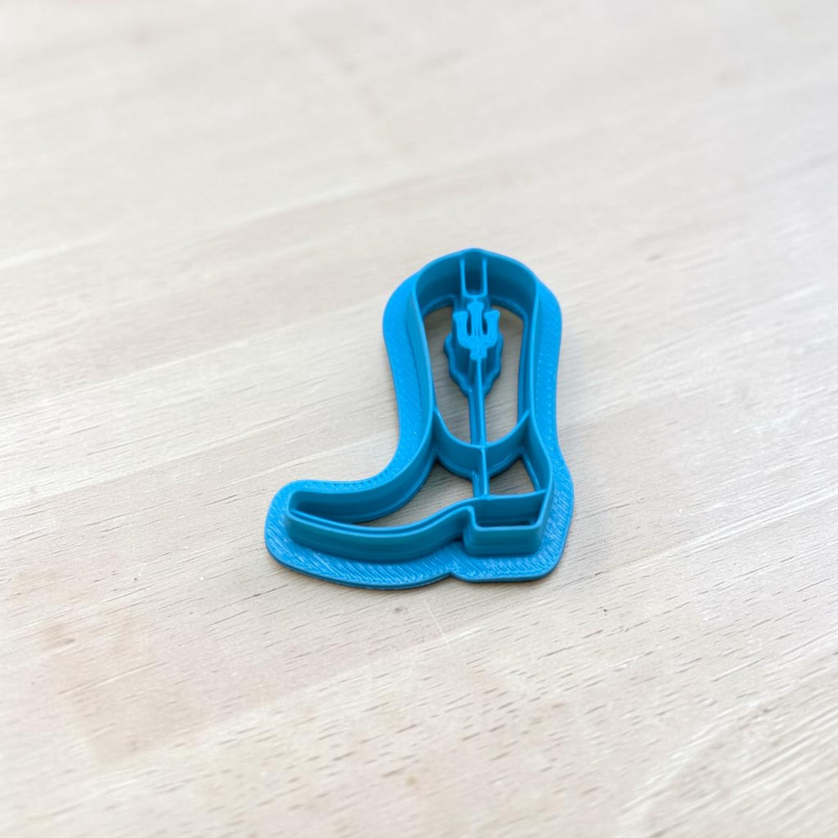 Blue 3D-printed Indiana-inspired cowboy boot cookie cutter featuring western boot details and a decorative emblem on the shaft, photographed on light wood for cookies, polymer clay earrings, fondant and crafts.
