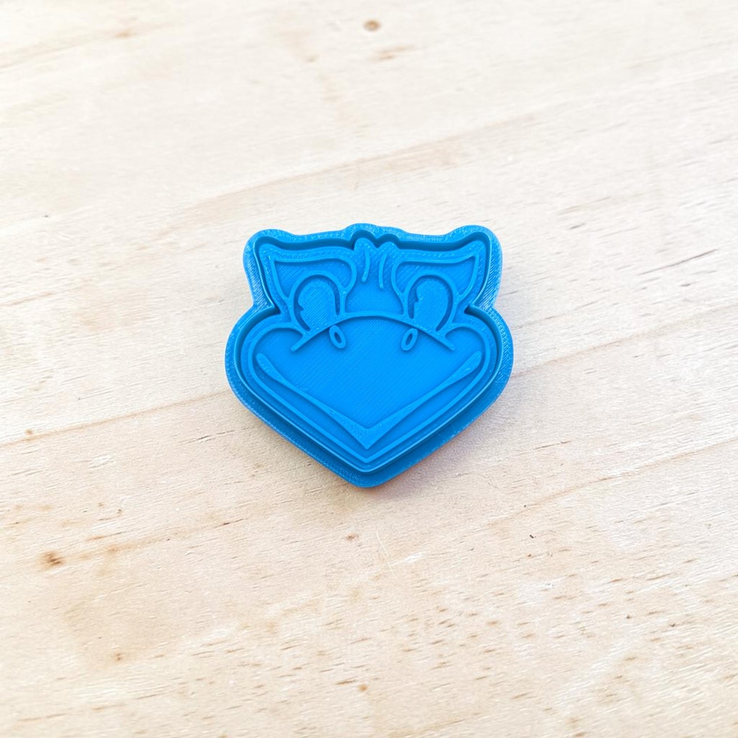 Blue cookie cutter shaped like a Jayhawks face on a light wooden surface