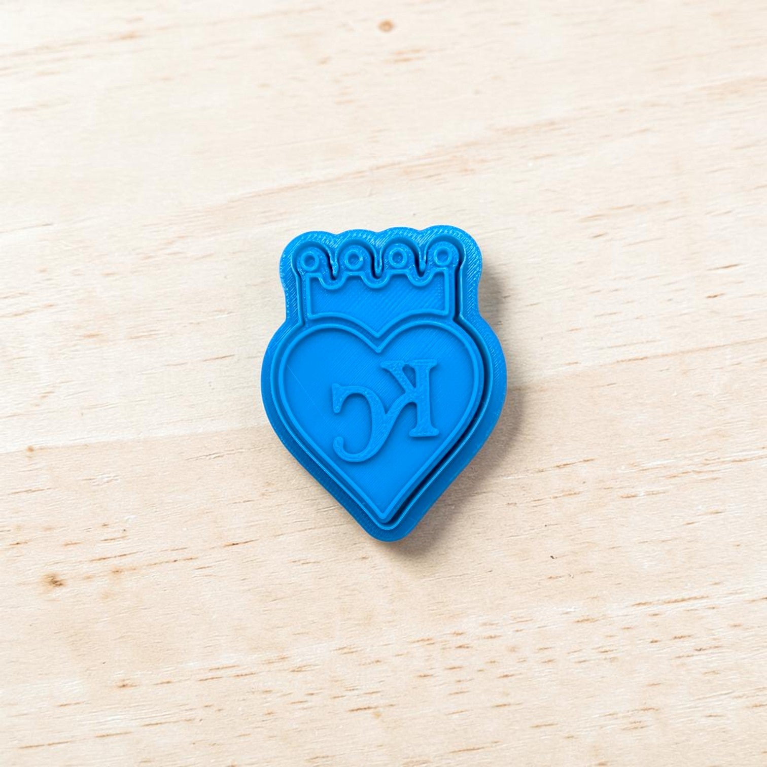 Blue heart-shaped cookie cutter with 'KC' initials on a light wood surface