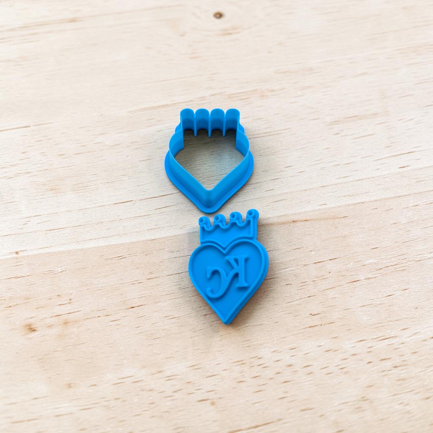 Two blue cookie cutters shaped like a heart with a crown and a diamond on a wooden surface.