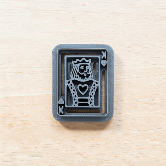 A 3D-printed gray playing card 'King of Hearts' stamp or mold, shown from a top-down view on a light wood grain surface.