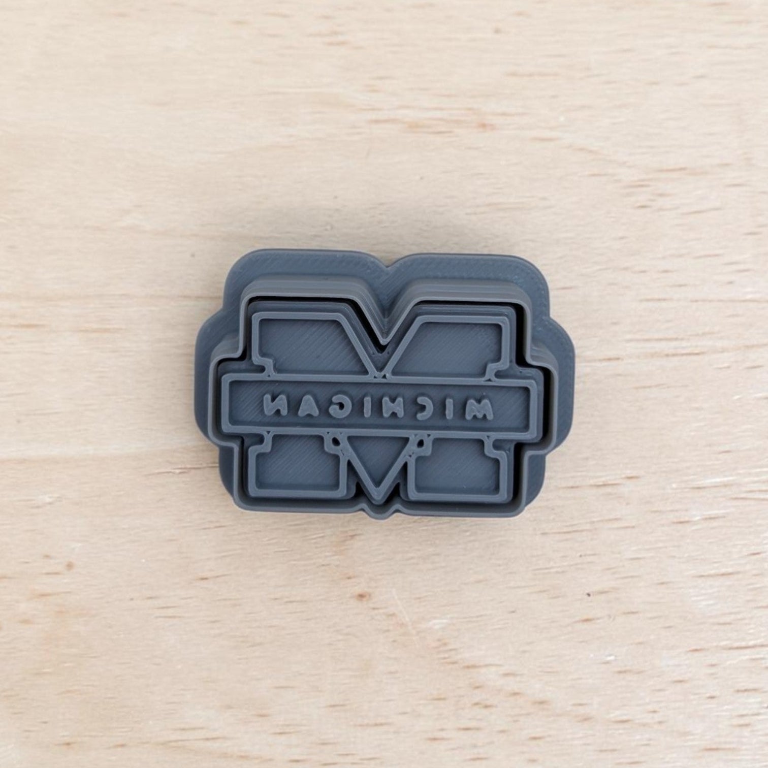 Michigan Wolverines M cookie cutter and embossing stamp for cookies, fondant, and polymer clay — gray 3D printed baking tool on wood background.