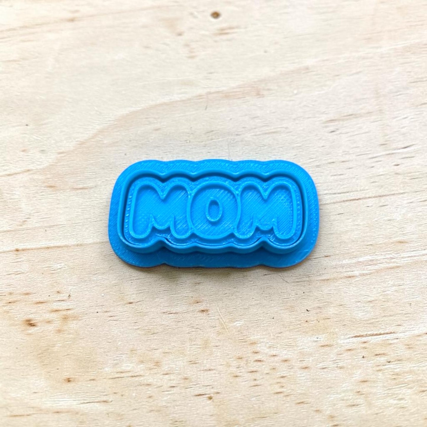 Blue 'MOM' cookie cutter on a wooden surface
