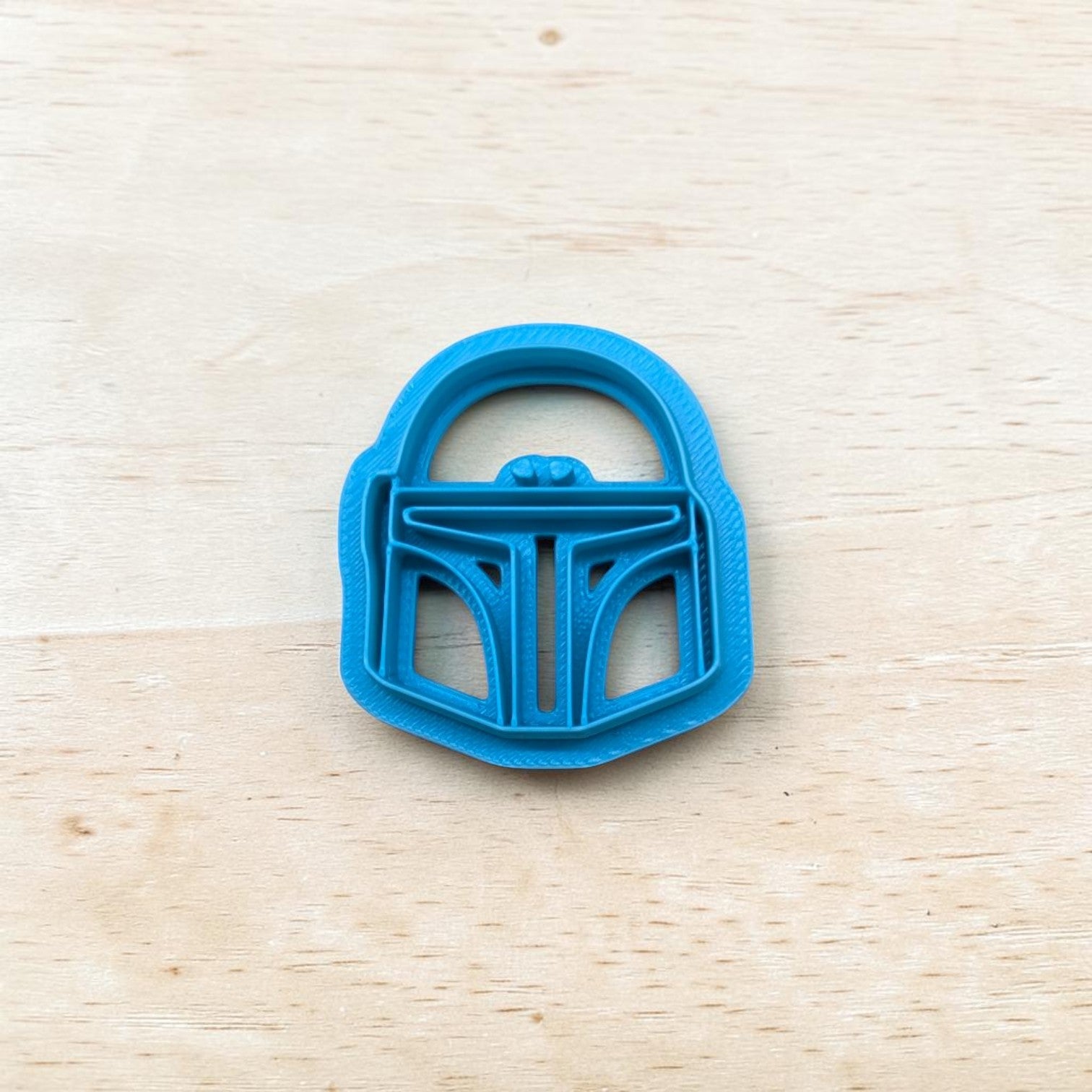 Blue cookie cutter shaped like a Boba Fett helmet 
on a wooden surface