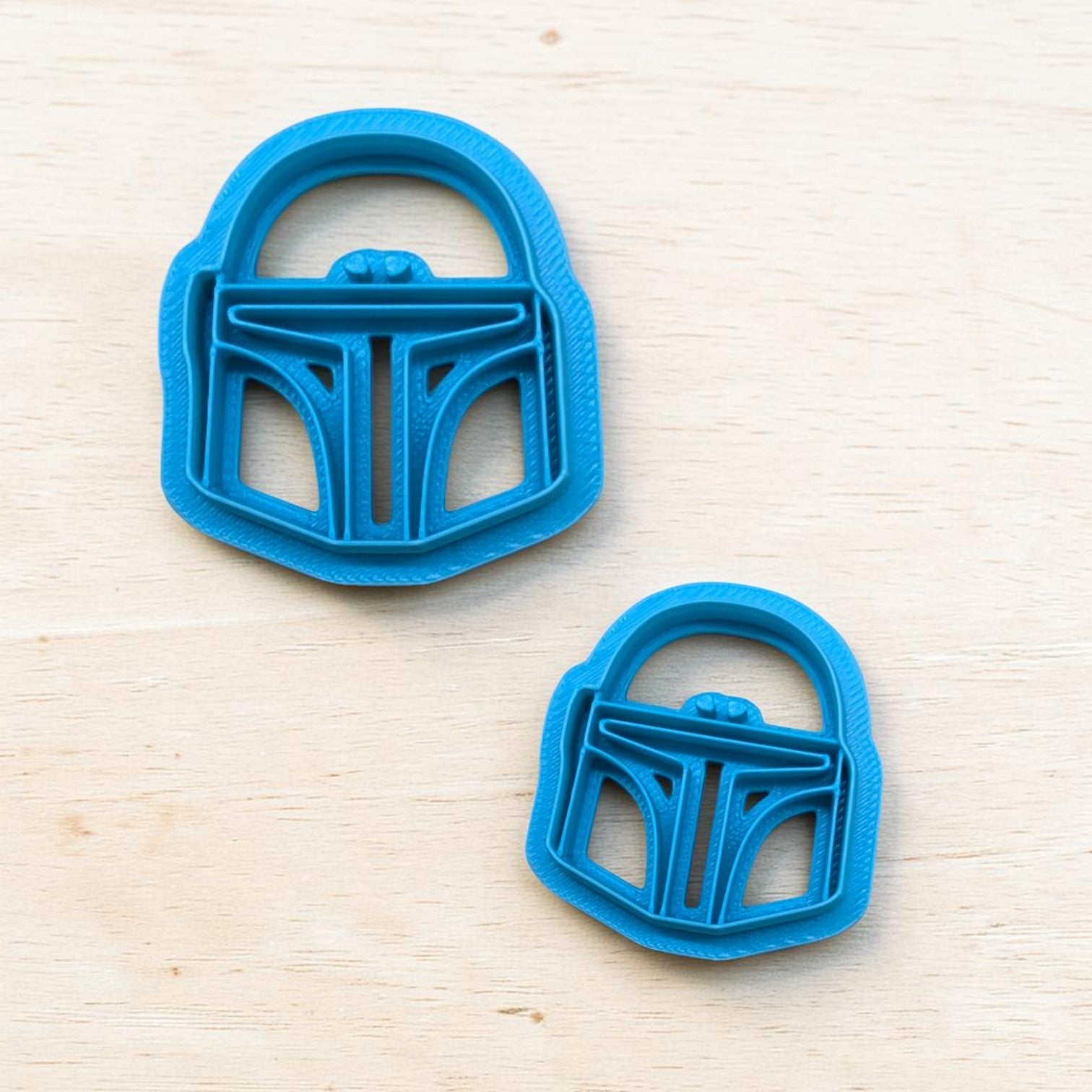 Two blue cookie cutters shaped like helmets on a light wood surface