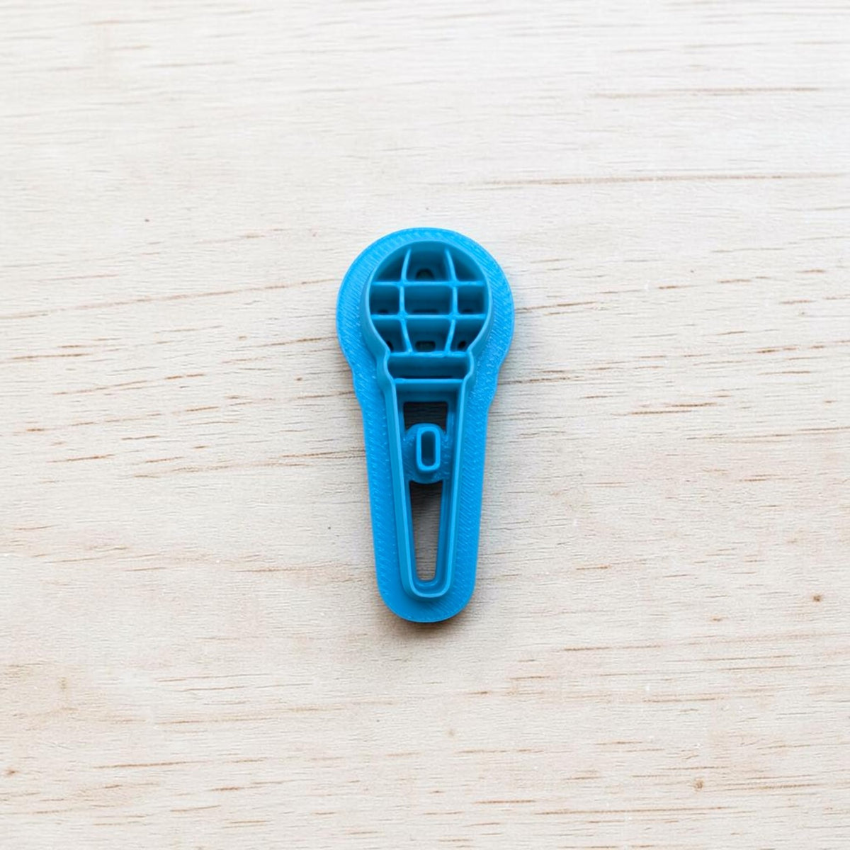 Blue microphone‑shaped cookie cutter on light wooden background — polymer clay and fondant tool by Truley Unique.