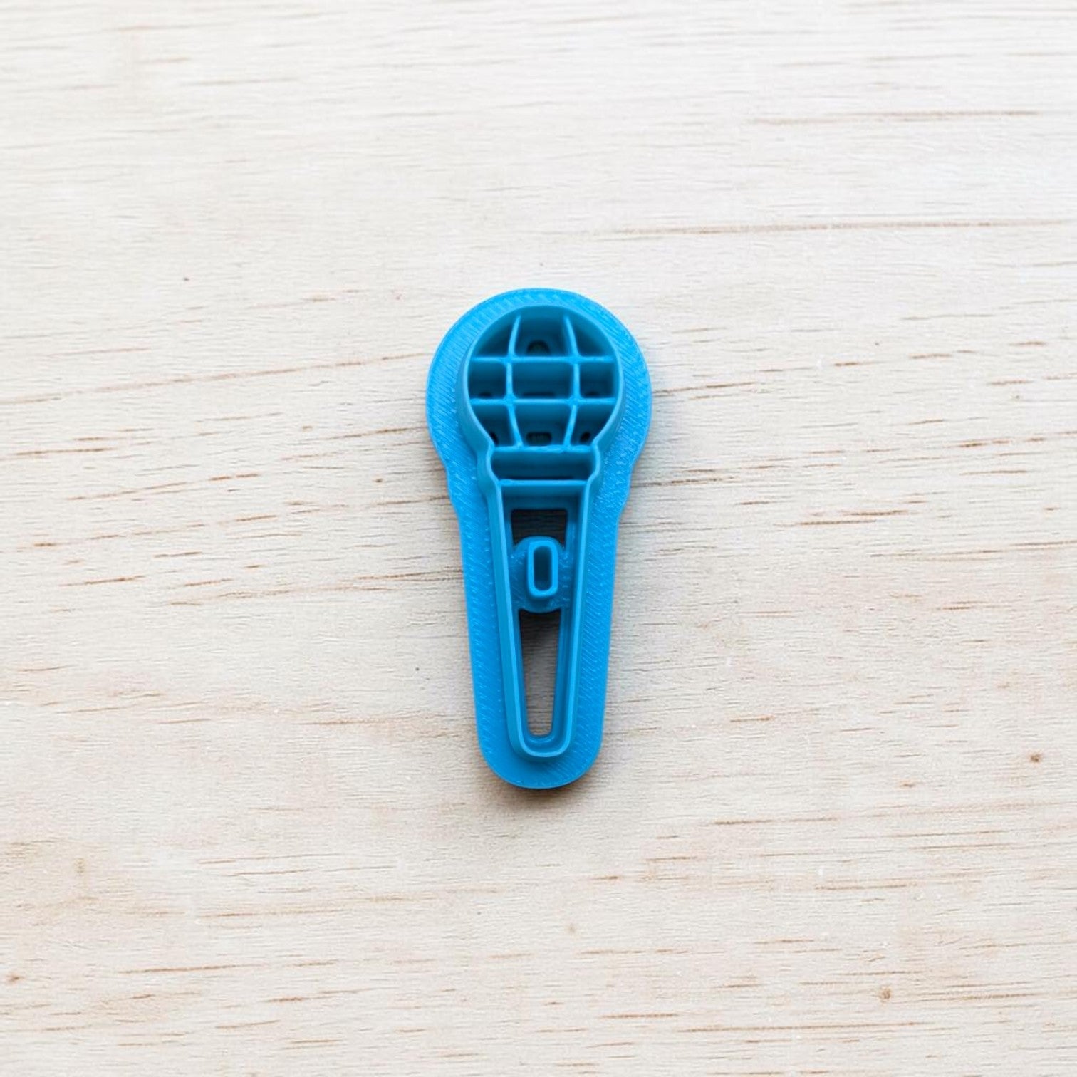 Blue microphone‑shaped cookie cutter on light wooden background — polymer clay and fondant tool by Truley Unique.