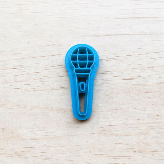 Blue microphone‑shaped cookie cutter on light wooden background — polymer clay and fondant tool by Truley Unique.
