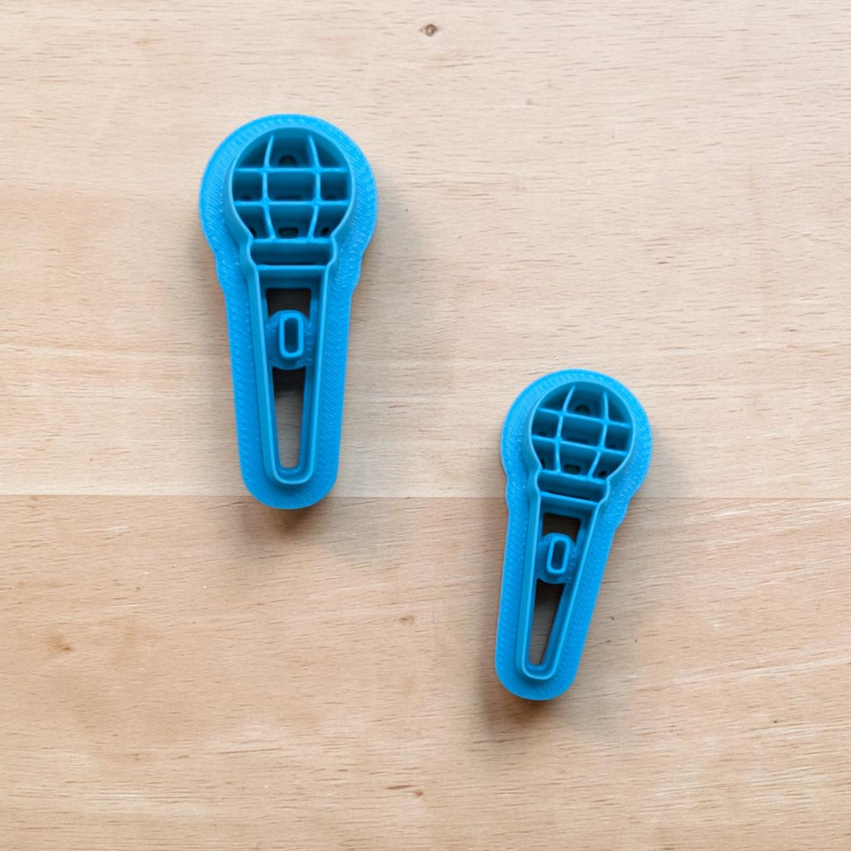 Two blue microphone cookie cutters in different sizes on wooden surface — 3D‑printed baking and pottery tools from Truley Unique