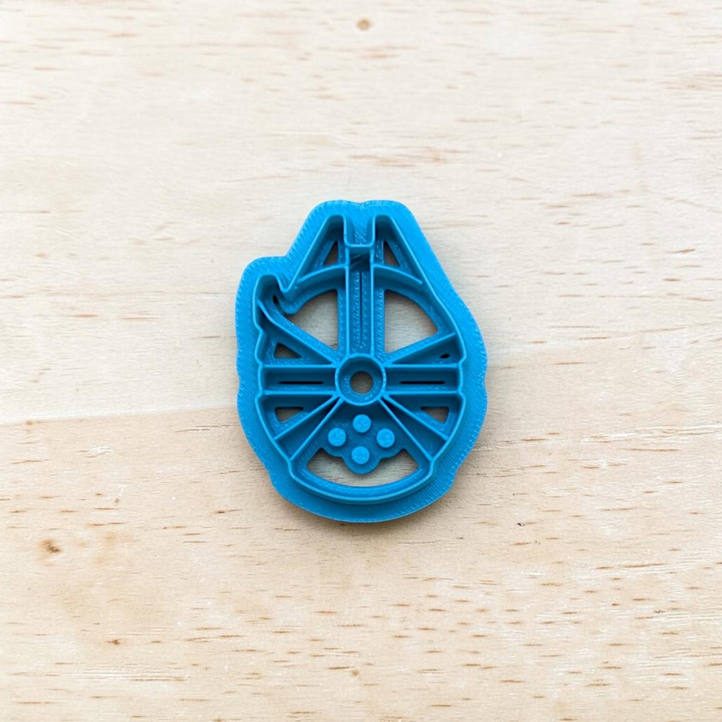 Plastic Millennium Falcon spaceship shape cookie cutter on a light color wood surface.