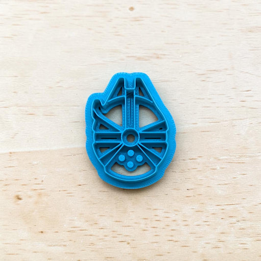 Plastic Millennium Falcon spaceship shape cookie cutter on a light color wood surface.