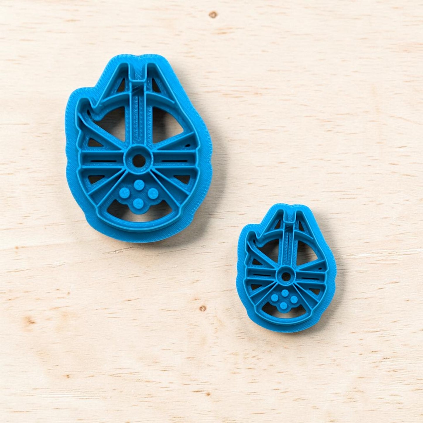 Plastic Millennium Falcon spaceship shape cookie cutters on a light color wood surface.