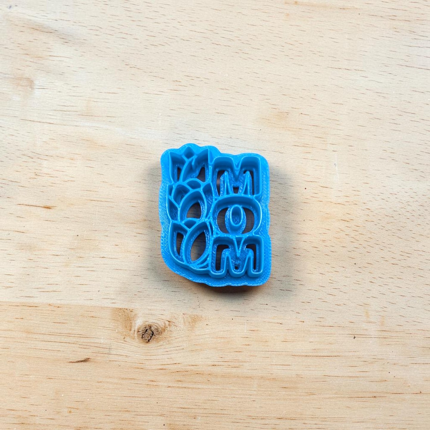 Blue cookie cutter with the text 'MOM' and tulips on a wooden surface