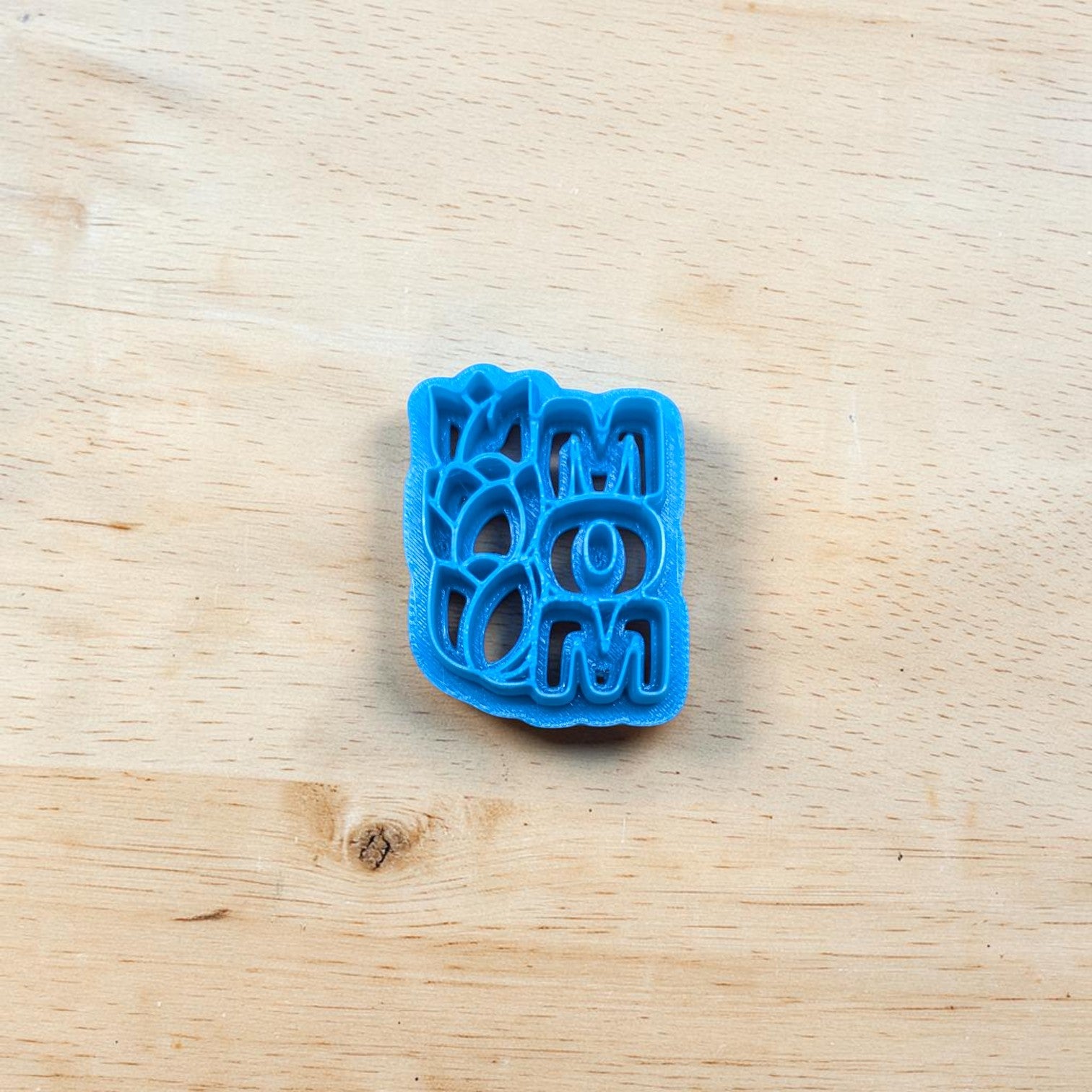 Blue cookie cutter with the text 'MOM' and tulips on a wooden surface