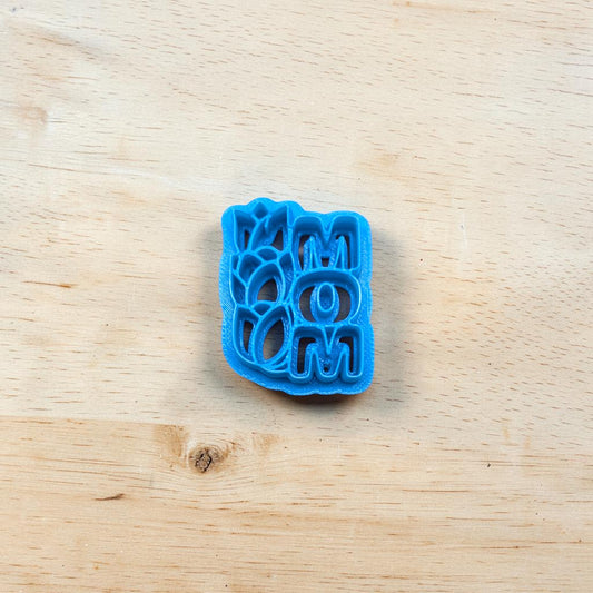 Blue cookie cutter with the text 'MOM' and tulips on a wooden surface