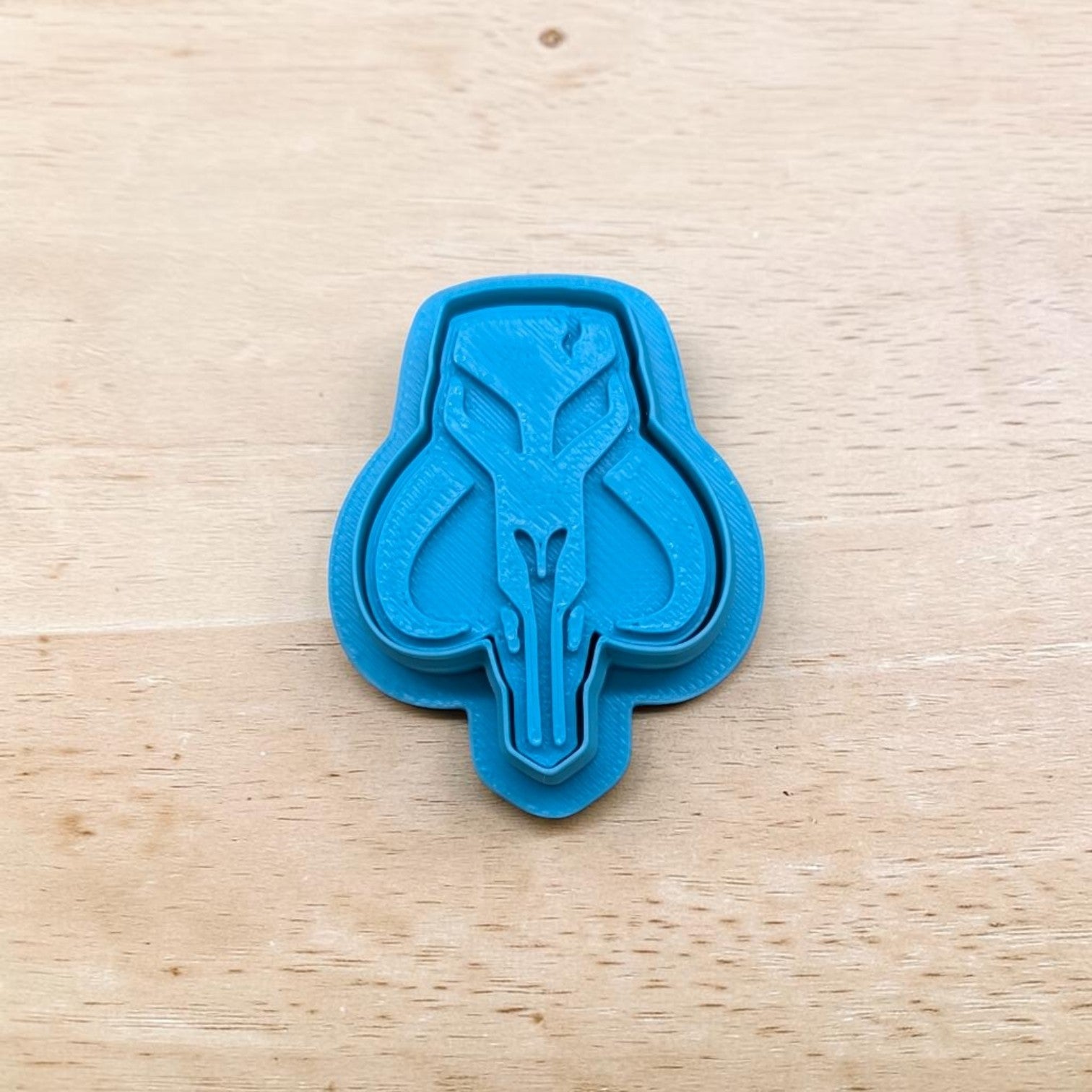 Blue cookie cutter shaped like a Mandalorian Mythosaur Skull on a wooden surface