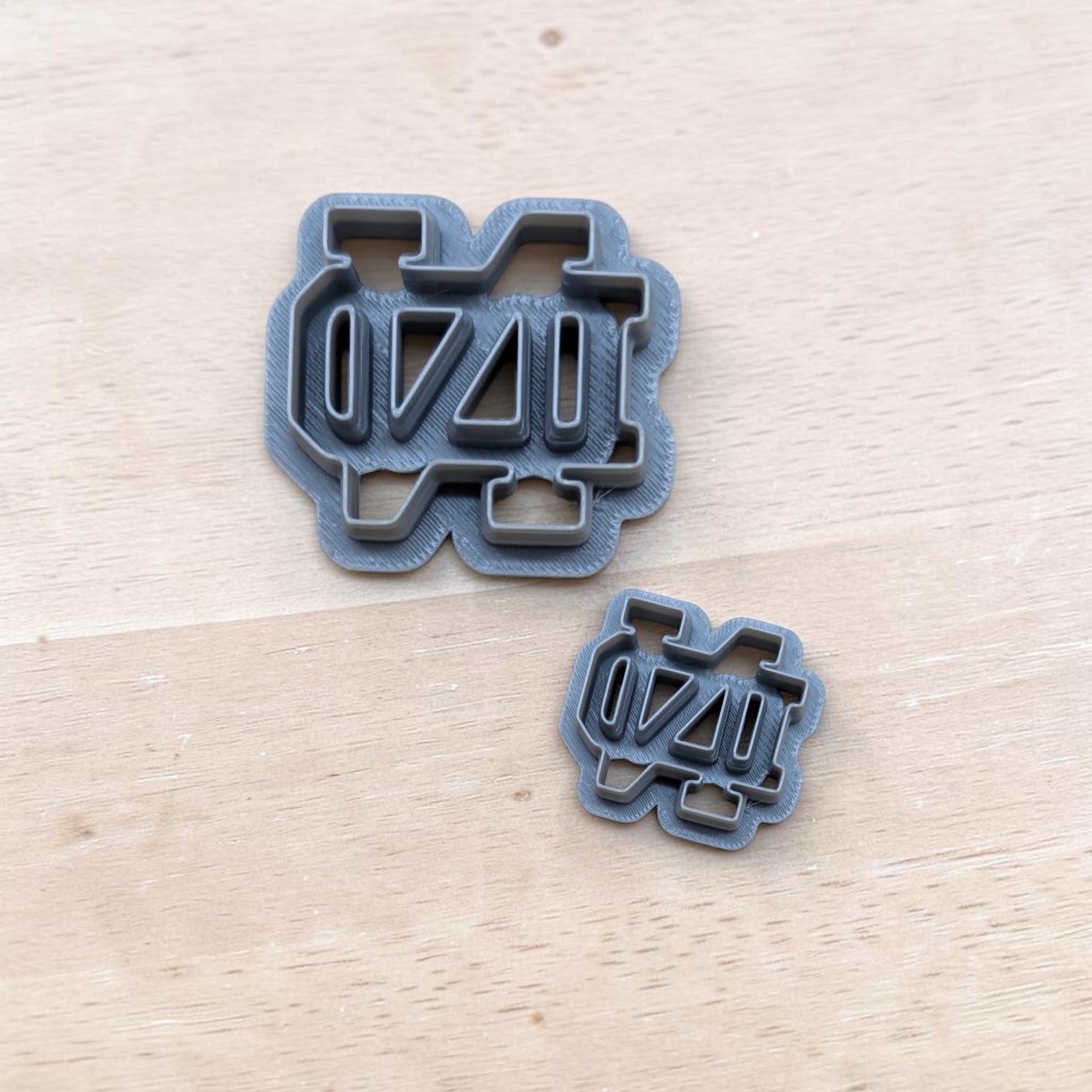 Two gray Notre Dame ND cookie cutters in different sizes on light wood background — durable 3D‑printed tools for cookies, fondant, and clay crafting.