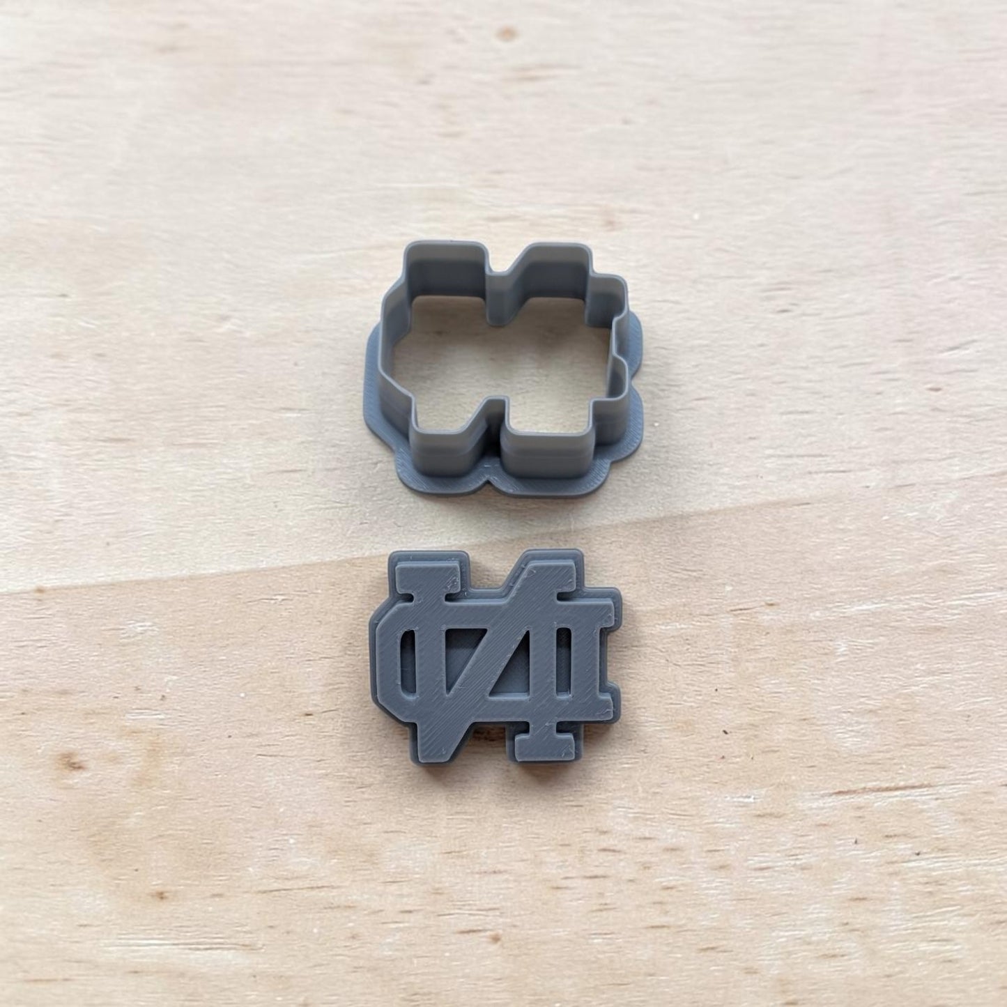 Two‑piece ND‑inspired cutter and stamp set, 3D‑printed gray plastic, displayed on wooden background for baking and crafting.